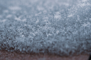 Macro photography of snow crystals. Frozen water, symmetrical shape, snowflake closeup. Natural texture. Selective focus on the details, blurred background.
