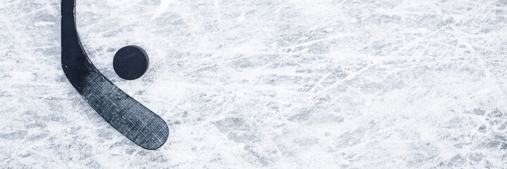 Old black hockey stick and rubber puck on ice background. Closeup. Wide banner. Empty place for...