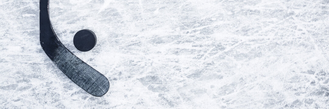 Old black hockey stick and rubber puck on ice background. Closeup. Wide banner. Empty place for text. Top down view.