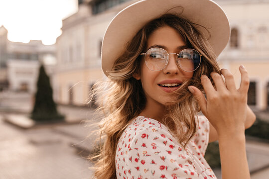 Close-up caucasian young european woman looking to side outdoors. Blonde in transparent round glasses with flying hair in wind in beige hat. People and free time concept