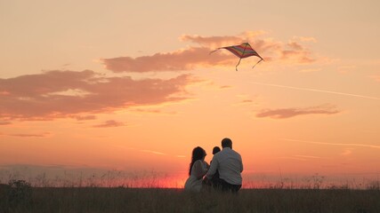 cheerful child launches kite with parents at sunset, little kid plays with father and mother in the light of sun, boy son with mom and dad happy family, joyful weekend life in nature outdoor travel