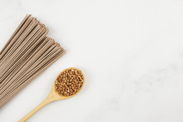 Dry Soba buckwheat noodles and wooden spoon with buckwheat on a light marble top. Banner about traditional Japanese food, Asian food and healthy eating. Culinary template for adding text.