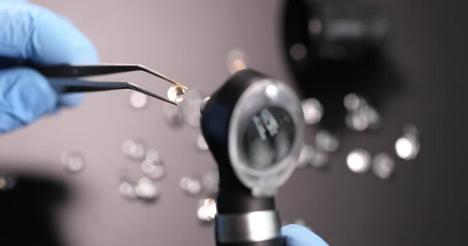 Gloved jeweler holds tweezers with gem and examines through magnifying glass slow motion 4k movie