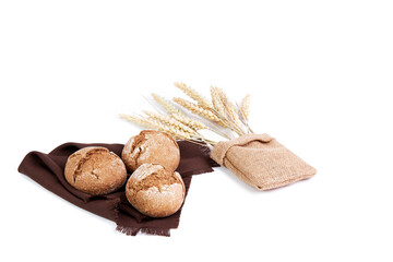 Rye bread baguettes on a brown cloth next to some ears of wheat inside a raffia bag on a white background
