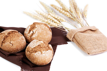 Rye bread baguettes on a brown cloth next to some ears of wheat inside a raffia bag on a white background