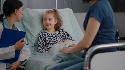Mother sitting with sick little daughter recovering after medical surgery during sickness examination in hospital ward. Pediatrician woman doctor explaining antibiotics treatment monitoring disease