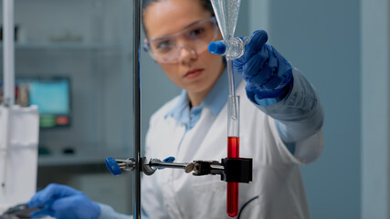 Close up of scientist using laboratory glassware on desk for medical experiment. Biochemistry doctor mixing blood in test tube with solution from chemical dripping pipe for development