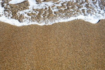 sea background surf with foam on sandy beach top view, horizontal.