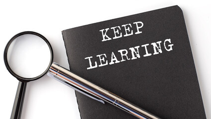 KEEP LEARNING - business concept, magnifier with white text message on black notebook