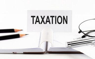 TAXATION on paper card,pen, pencils, glasses,financial documentation on table - business concept