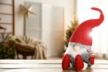 Fototapeta premium Funny Christmas gnome on wooden table in room with festive decorations. Space for text