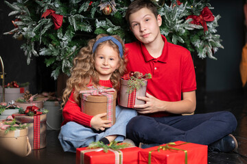Obraz na płótnie Canvas little girl and boy, sister and brother in red clothes with gifts near Christmas tree. Smiling children waiting santa for new year. Happy family winter holiday. Christmas kids with gift
