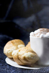A cup of steamed coffee and a croissant on a dark background