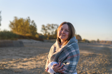 Woman wrapping up with big wool scarf walking on beach at cold morning sunrise