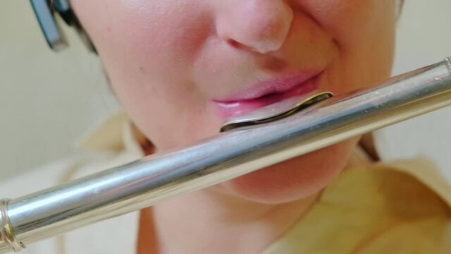 A woman lips with a flute is playing at home on the sofa in the living room, close-up
