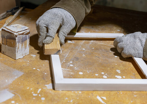 Close-up of a wooden frame that a hobbyist smoothes with sandpaper