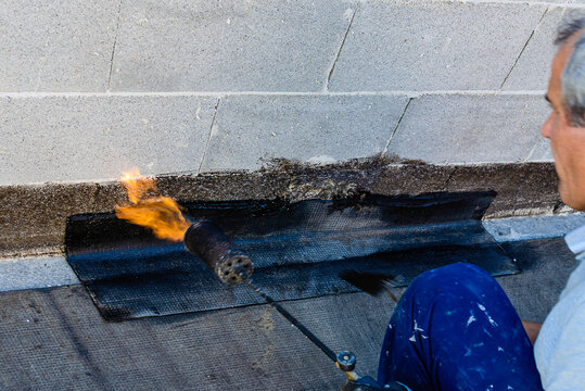 Propane blowtorch at floor slab insulation work. Flat roof covering works with roofing felt