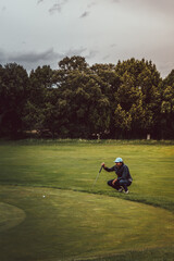 Golfer crouching looking at ball on green with forest in background