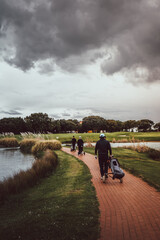 Players walking across a bridge between lakes on a golf course on a cloudy day