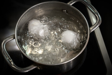 Two white eggs are boiled in a saucepan.
