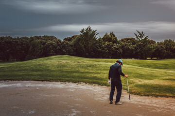 Golfer walking through the bunker on a golf course on a cloudy day