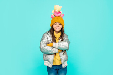 happy teen girl with toy bear crossed hands. child wear warm clothes on blue background.
