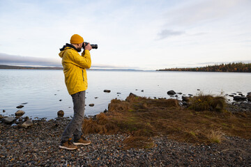 Professional nature photographer taking photo of lake wearing bright yellow coat