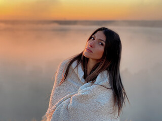 Woman standing with white plaid on the mountain top looking at panoramic view of mountain range in the mist under the sunrise
