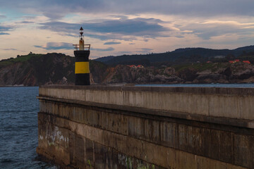 Black and yellow lighthouse in the harbor with the sea and mountains in the background