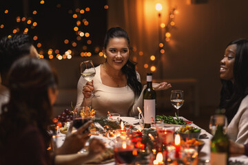 holidays, party and celebration concept - multiethnic group of happy friends having christmas dinner at home and drinking wine