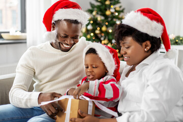 family, winter holidays and people concept - happy african american mother, father and little son opening gift box at home on christmas