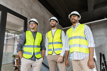 architecture, construction business and people concept - happy smiling male architects in helmets and reflective safety wests at office
