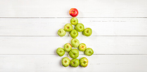 Naklejka na ściany i meble Edible Xmas tree of green apples with red apple as star on white wooden table. Banner. Copy space.