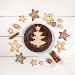 Baking as Xmas tree on brown plate, star shape cookies, walnuts, cinnamon on white wooden table.
