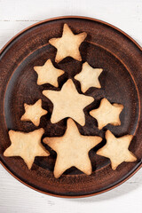 Top view homemade star shape cookies laid out as creative Xmas tree on round brown plate close up.