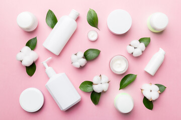 Organic cosmetic products with cotton flower and green leaves on color background. Flat lay