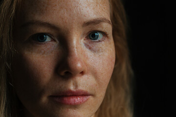Beautiful woman with read hair and freckles. Close up portrait against black background