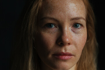 Beautiful woman with read hair and freckles. Close up portrait against black background