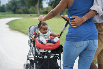 African family walking with kid on stroller outdoor at park city - Focus on father hand