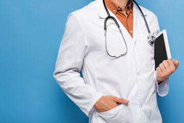 cropped view of doctor in white coat standing with hand in pocket and holding digital tablet with blank screen on blue