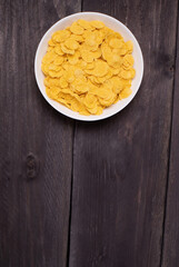 Cornflakes in a brown clay plate on a shabby wooden background, space for text