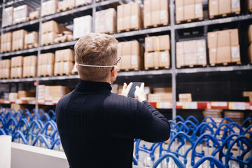 Young manager of store, man worker with protective mask using phone working in industrial factory or warehouse