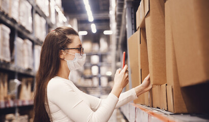 Woman warehouse worker in protective mask with phone scan cardboard box, service delivery