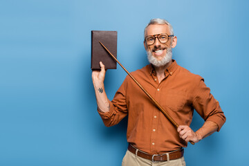 happy middle aged teacher in glasses holding pointer stick near book on blue