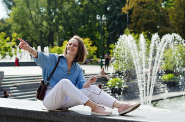 Urban portrait of young attractive business woman in eye glasses and casual clothes. Woman walking in the city street, park, talking on her phone, making selfie, works in sunny day.