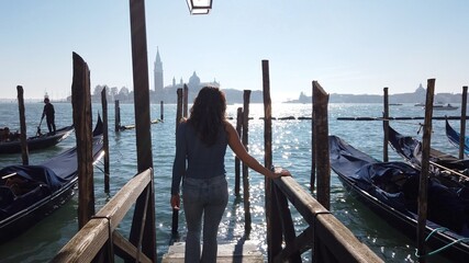 Europe, Italy - young girl walks on the wooden deck of gondola boats in the Venice lagoon on a...