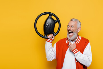 amazed middle aged man in bomber jacket pointing at steering wheel on yellow