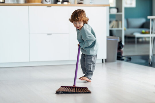 Little cute boy sweeping and cleaning the floor of the kitchen at home.