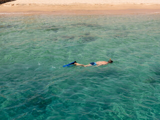 Man with a snorkel, mask and fins swims in the azure water of the Red Sea.