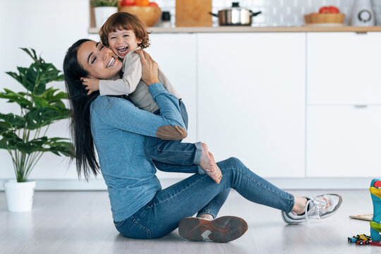 Young beautiful mother playing and having fun on the floor with her son in living room at home.